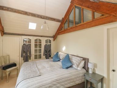 A bedroom with a bed side table and chair with robes hanging on a wardrobe at The Coach House Merrion near Pembroke
