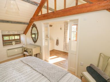 A bedroom with a bed a dressing table an oval mirror and a chair next to a doorway leading to a bathroom at The Coach House in Merrion near Pembroke