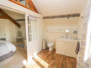 A bathroom with a toilet and sink next to a bedroom with a bed and chair at The Coach House Merrion near Pembroke