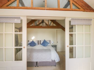 A bedroom with a double bed and bedside tables seen through sliding glass doors at The Coach House Merrion near Pembroke