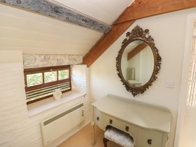 A small room with a window a radiator an ornate oval mirror a desk and a stool at The Coach House Merrion near Pembroke