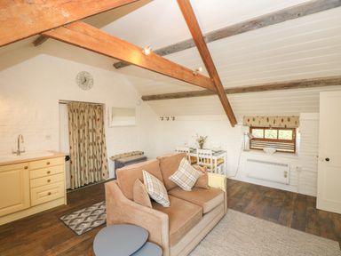 A living room with a sofa and cushions a small dining table with chairs exposed wooden beams a window with a blind and a kitchenette at The Coach House Merrion near Pembroke