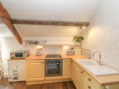A kitchen with wooden cabinets a stove oven microwave kettle toaster bread bin and a sink at The Coach House Merrion near Pembroke