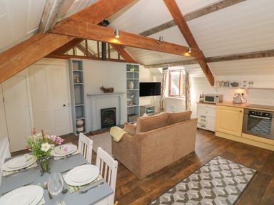A dining table set with plates and cutlery in an open living room and kitchen with exposed wooden beams and a sofa at The Coach House in Merrion near Pembroke