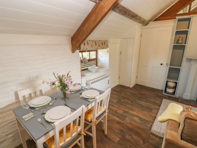A dining area with a table set for four next to a window in a room with wooden floors and exposed ceiling beams at The Coach House in Merrion near Pembroke