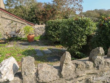 A small courtyard with stone walls a potted plant a round table and chairs at The Coach House in Merrion near Pembroke