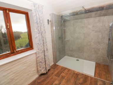 A bathroom with a glass shower enclosure wooden floor and a window with curtains at The Coach House in Merrion near Pembroke