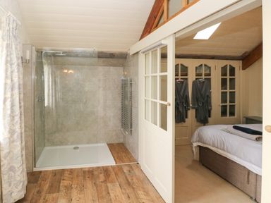 A bathroom with a walk in shower next to a bedroom with a bed and robes hanging on closet doors at The Coach House Merrion near Pembroke