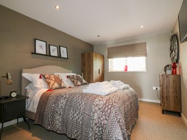 A bedroom with a bed with patterned bedding and folded towels bedside tables a wooden wardrobe a window and a wooden dresser at The Bolt Hole in Downderry