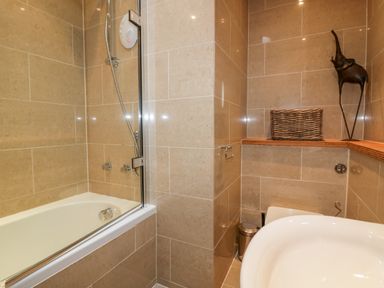 A bathroom with a bathtub shower and wicker basket on wooden shelf at The Bolt Hole in Downderry