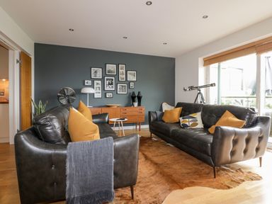 A living room with two black leather sofas and orange pillows at The Bolt Hole in Downderry