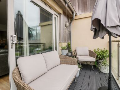 An outdoor balcony with wicker sofa and chair with cushions umbrella and potted plants at The Bolt Hole in Downderry