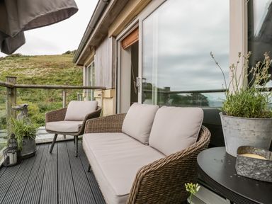 An outdoor balcony with wicker sofa and chair with cushions and plants at The Bolt Hole Downderry