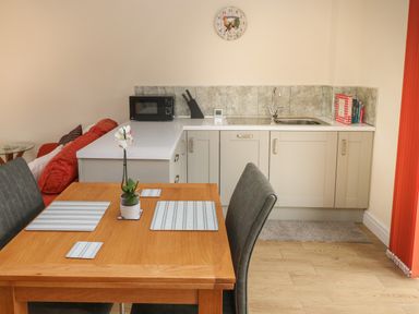 A kitchen and dining area with a wooden table set with placemats and a potted plant at Nuthatch Barn in Hensol near Pontyclun
