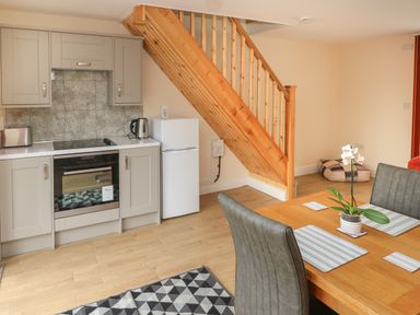 A kitchen with oven fridge and kettle under wooden staircase next to a dining table with chairs and a plant at Nuthatch Barn in Hensol near Pontyclun
