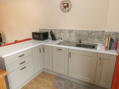 A kitchen corner with grey cabinets a stainless steel sink microwave oven knife block and cookbooks at Nuthatch Barn in Hensol near Pontyclun