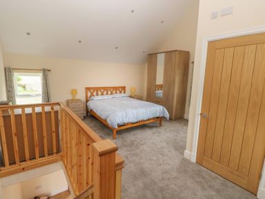 A bedroom with a bed bedside tables lamps a wardrobe window and a wooden staircase at Nuthatch Barn in Hensol near Pontyclun