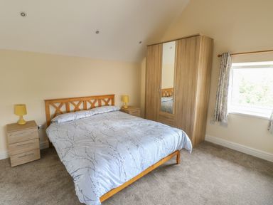 A bedroom with a double bed flanked by two bedside tables with yellow lamps and a wardrobe with a mirror at Nuthatch Barn in Hensol near Pontyclun