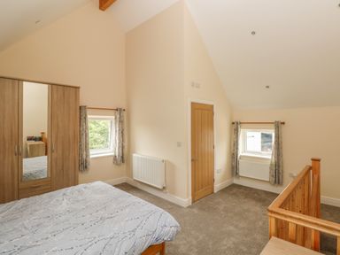 A bedroom with a bed wardrobe wooden door two windows and a wooden staircase railing at Nuthatch Barn Hensol near Pontyclun