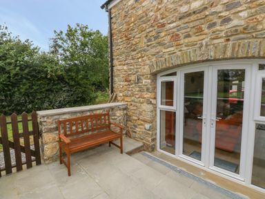 An outdoor patio with a wooden bench next to a stone wall and white double doors at Nuthatch Barn in Hensol near Pontyclun