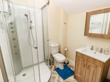 A bathroom with a shower enclosure toilet with blue rug and wooden vanity unit with mirror at Nuthatch Barn Hensol near Pontyclun