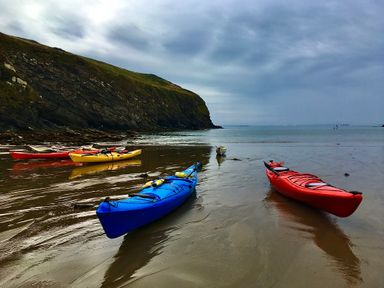 Several kayaks on the wet sand near a rocky cliff and calm sea at Y Twll Bollt (The Bolt Hole) in Folkeston Hill Nolton Haven West Wales & Pembrokeshire