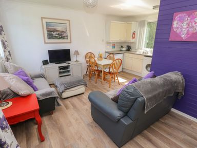 A living room with two sofas a television on a cabinet a dining table with four chairs and a kitchen area with cabinets and appliances at Y Twll Bollt The Bolt Hole Folkeston Hill Nolton Haven West Wales and Pembrokeshire