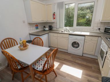A kitchen with a dining table and chairs washing machine microwave and a window at Y Twll Bollt The Bolt Hole in Folkeston Hill Nolton Haven West Wales Pembrokeshire