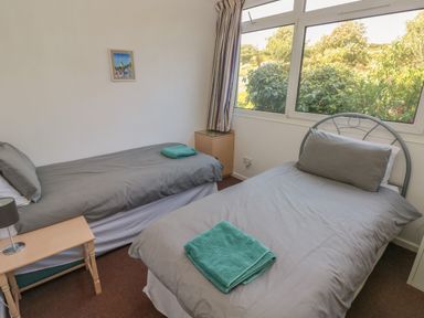 A bedroom with two single beds gray bedding green towels a small wooden table with a lamp and a window with a view of greenery at Y Twll Bollt The Bolt Hole Folkeston Hill Nolton Haven West Wales and Pembrokeshire