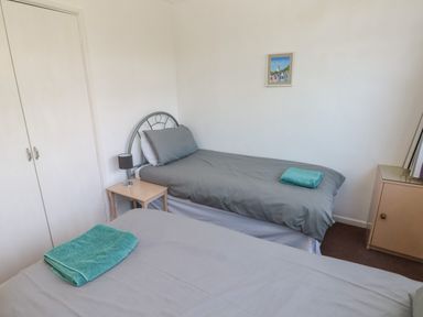 A bedroom with two single beds a bedside table with a lamp a framed picture on the wall and a cupboard at Y Twll Bollt (The Bolt Hole) Folkeston Hill Nolton Haven West Wales and Pembrokeshire