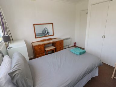 A bedroom with a bed, wooden desk with mirror, small stool, white wardrobe, and bedside lamp at Y Twll Bollt The Bolt Hole in Folkeston Hill Nolton Haven West Wales Pembrokeshire