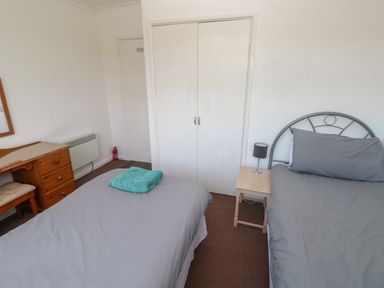 A bedroom with two single beds, a wooden dresser with a mirror, a small bedside table with a lamp, and a closet with white doors at Y Twll Bollt (The Bolt Hole) in Folkeston Hill, Nolton Haven, West Wales & Pembrokeshire