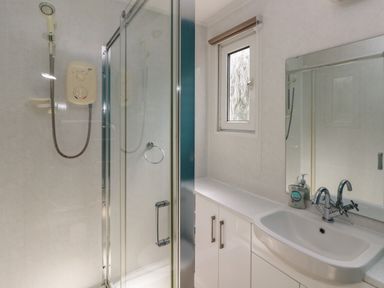 A bathroom with a shower enclosure, window, sink with faucet, mirror, and cabinet at Y Twll Bollt (The Bolt Hole) in Folkeston Hill, Nolton Haven, West Wales & Pembrokeshire
