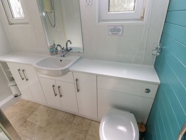 A bathroom with a sink, white cabinets, a toilet, and a blue paneled wall at Y Twll Bollt (The Bolt Hole) in Folkeston Hill, Nolton Haven, West Wales & Pembrokeshire