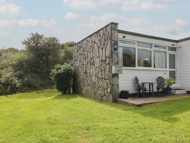 A small patio with two chairs and a table outside a house with stone and white panel walls at Y Twll Bollt The Bolt Hole in Folkeston Hill Nolton Haven West Wales Pembrokeshire