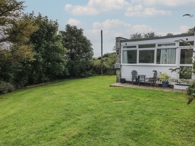 A grassy garden area with trees and a small patio with chairs and table outside a white house at Y Twll Bollt in Folkeston Hill Nolton Haven West Wales and Pembrokeshire