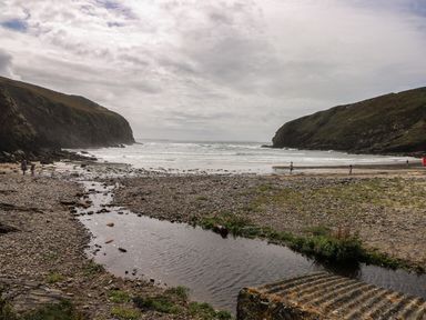 A rocky beach with a small stream flowing into the sea and hills on both sides at Y Twll Bollt The Bolt Hole in Folkeston Hill Nolton Haven West Wales and Pembrokeshire