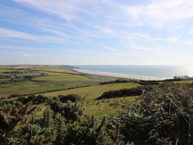 A coastal landscape with fields houses and a beach along the sea at Y Twll Bollt The Bolt Hole in Folkeston Hill Nolton Haven West Wales and Pembrokeshire