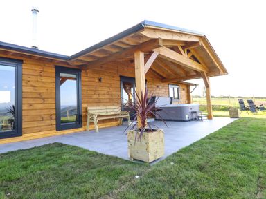 An outdoor patio area with a wooden bench hot tub two planters and two black chairs at Bacheiddon Log Cabin Aberhosan near Machynlleth