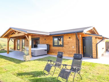 A wooden cabin with a hot tub and two reclining chairs outside on grass at Bacheiddon Log Cabin in Aberhosan near Machynlleth