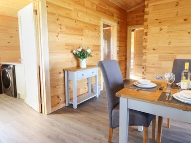 A dining area with a table set for meals and a small table with flowers on it at Bacheiddon Log Cabin Aberhosan near Machynlleth