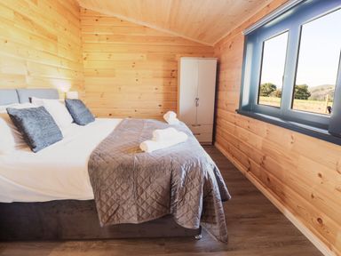 A bedroom with a bed linens and pillows next to a window and a white wardrobe at Bacheiddon Log Cabin Aberhosan near Machynlleth