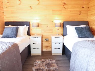 A bedroom with two single beds with gray headboards gray pillows white bedding and bedside tables with lamps at Bacheiddon Log Cabin Aberhosan near Machynlleth