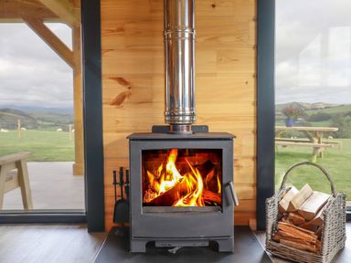 A wood burning stove with fire inside and a basket of firewood next to it at Bacheiddon Log Cabin in Aberhosan near Machynlleth
