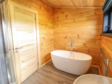 A bathroom with a freestanding bathtub wooden walls wooden door and a window at Bacheiddon Log Cabin in Aberhosan near Machynlleth