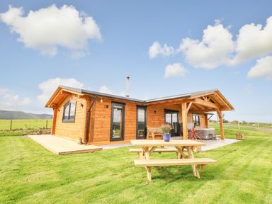 A wooden log cabin with a picnic table and plants on a lawn at Bacheiddon Log Cabin in Aberhosan near Machynlleth