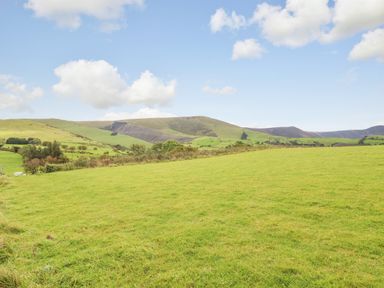 An open grassy field with hills and scattered trees under a partly cloudy sky at Bacheiddon Log Cabin Aberhosan near Machynlleth