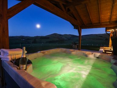 An outdoor covered hot tub with bubbling water towels bottle of champagne and glasses with hills in the background at Bacheiddon Log Cabin Aberhosan near Machynlleth