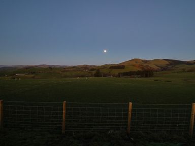 A rural landscape with green fields hills a wire fence and the moon in the sky at Bacheiddon Log Cabin Aberhosan near Machynlleth