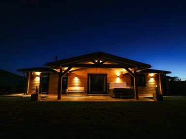 A wooden cabin with outdoor lights a bench and a hot tub at Bacheiddon Log Cabin Aberhosan near Machynlleth